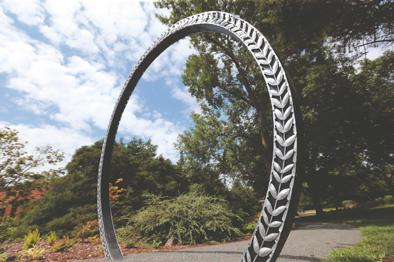 A circular metal archway with the shapes of barley at the entrance to a garden